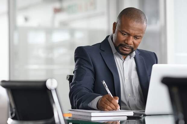 A person at a laptop holding a pen.