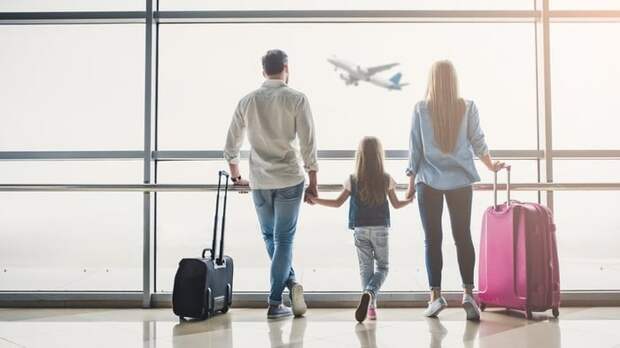 Mom, dad, and child stand next to luggage looking at airplane through an airport window
