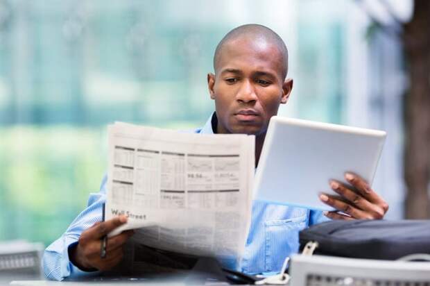 Man reading newspaper and looking at a tablet