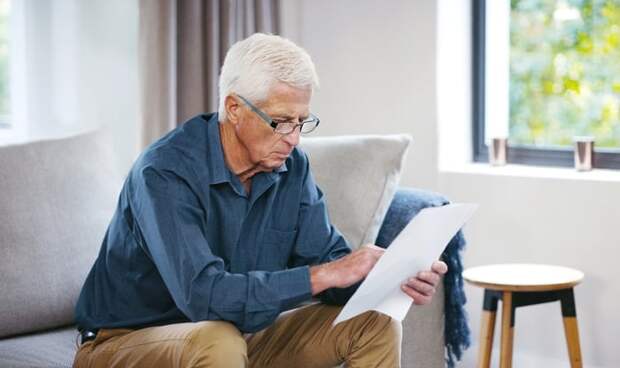 A person sitting on a couch and holding a document.
