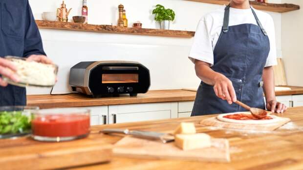 The Ooni Volt 12 electric pizza oven in a kitchen setting, with a pizza being put in the oven