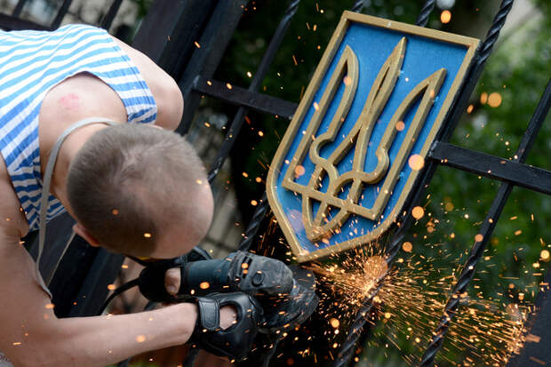 Боец ополчения Луганской народной республики срезает герб Украины с ворот здания областной администрации в Луганске. 
