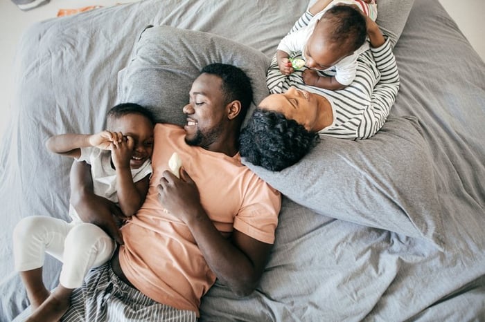 Two parents laying on their bed with their young children.