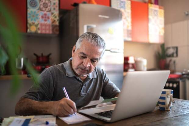 Person sitting in front of laptop and writing a note on a notepad.