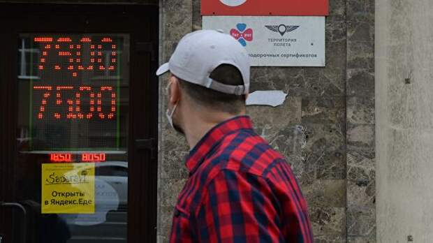 Мужчина в защитной маске у информационного табло с курсом валют на Тверской улице в Москве