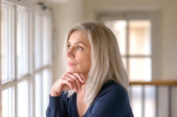 Person with a neutral expression looking out a window.