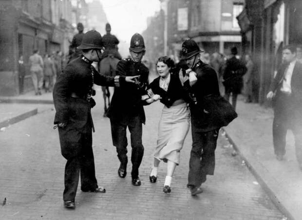 Полицейские арестовывают демонстрантку во время столкновения между коммунистами и британскими фашистами.