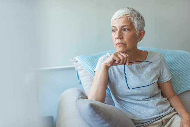 Worried person holding glasses and looking off into the distance.