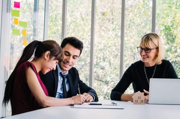 A smiling woman signing documents while sitting at a table with her husband and their realtor.