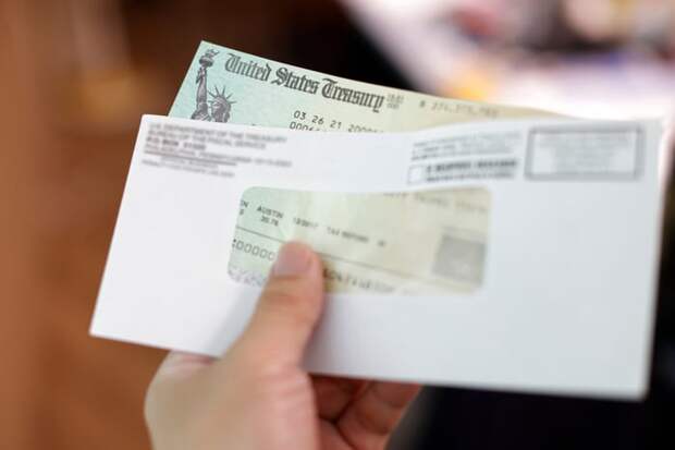 A person holding an envelope containing a check from the United States Treasury.