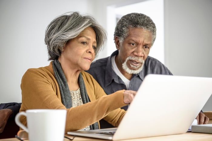Two people reading material on a shared laptop.