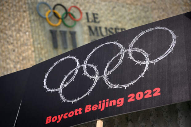 Табличка с изображением колючей проволоки, образующей Олимпийские кольца, рядом с вывеской Олимпийского музея во время протеста, организованного тибетскими и уйгурскими активистами против зимних Олимпийских игр 2022 года в Пекине, в Лозанне, Швейцария, 23 июня 2021 года. 