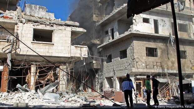 Люди около разрушенного здания в сирийской провинции Идлиб
