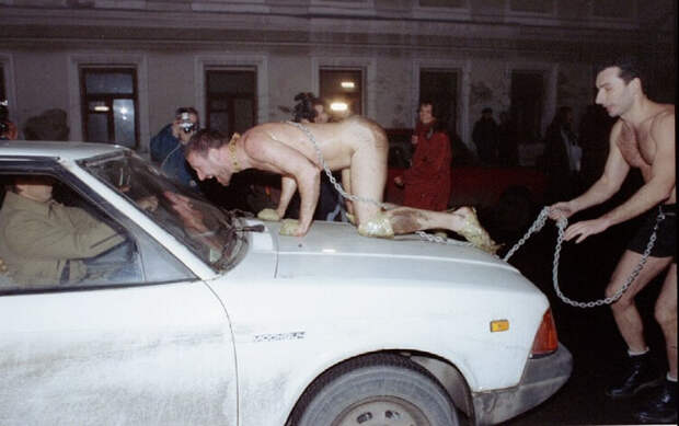 Russian artist Oleg Kulik imitating a dog, jumps on the car of a scared Muscovite as his colleague A..