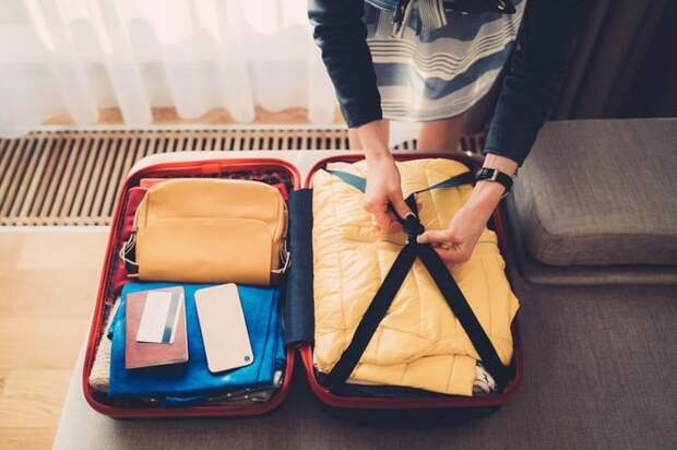 A woman packing a suitcase with her credit card, passport, and phone on top.