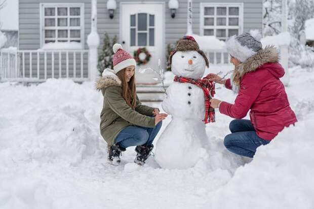 Mother and daughter building snowman in snowy yard