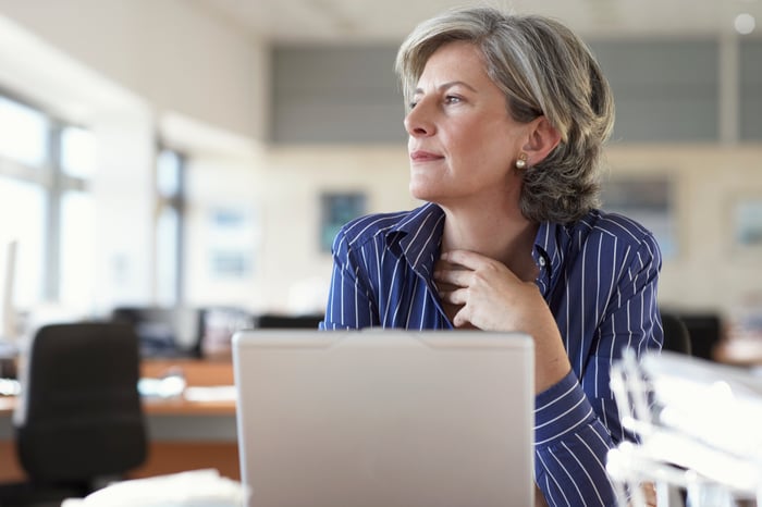 Person sitting in front of laptop, looking off as if in deep thought.