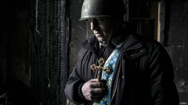 Украинский священник в каске держит крест