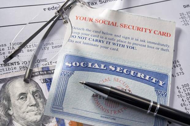 A Social Security card sitting under a pen with a $100 bill and glasses.