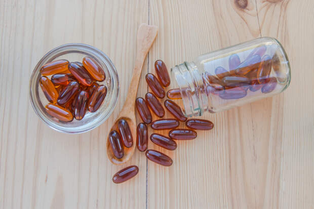 Lecithin gel vitamin supplement capsules in a cup, a spoon and a bottle on wooden table.