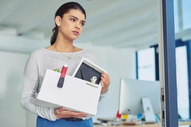 A young woman who was just let go from her job walking out of the office with a box of her things.
