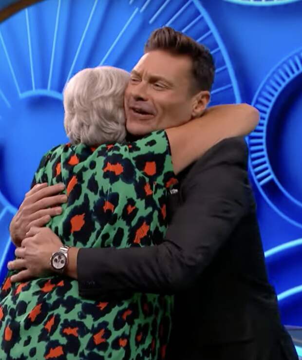 Ryan Seacrest embraced by a Wheel of Fortune contestant.