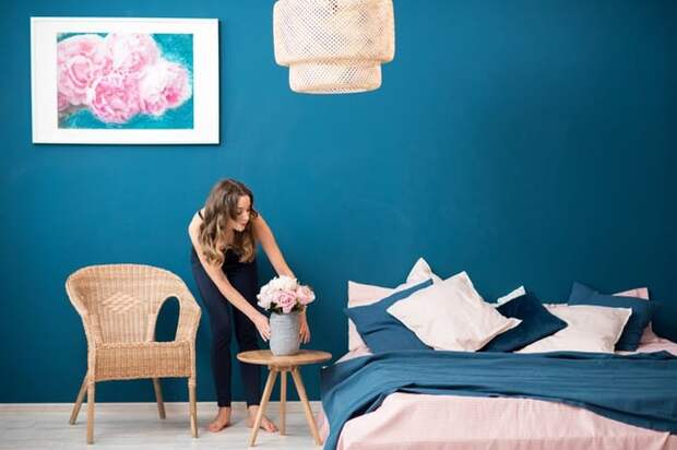 A woman arranging flowers on a bedside table in a well-decorated bedroom.