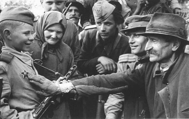 Командир стрелкового батальона В. Романенко (второй справа) рассказывает жителям одного из селений в районе Белграда о боевых делах юного разведчика – Вити Жайворонка. Старчево, Югославия, октябрь 1944
