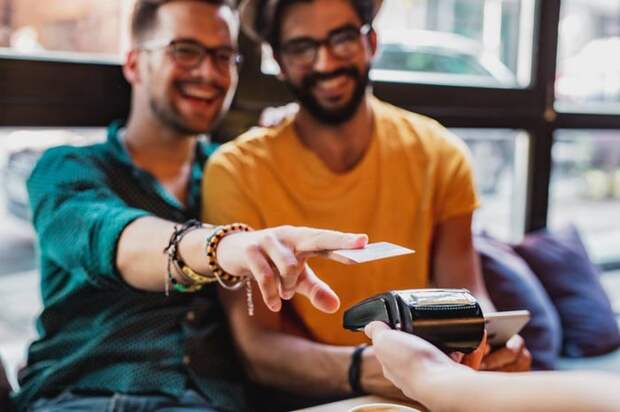 A couple smiles as they use a contactless credit card reader in a restaurant.