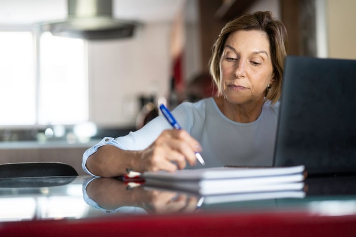 A person at a laptop is holding a pen.