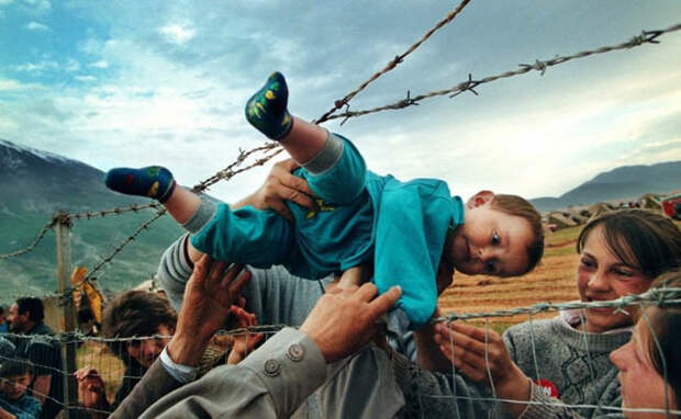 Маленького ребенка передают через колючую проволоку его бабушке и дедушке, которые находятся в лагере для беженцев, во время войны в Косово (2000 г.) подборка фото, хорошие фото, эмоции