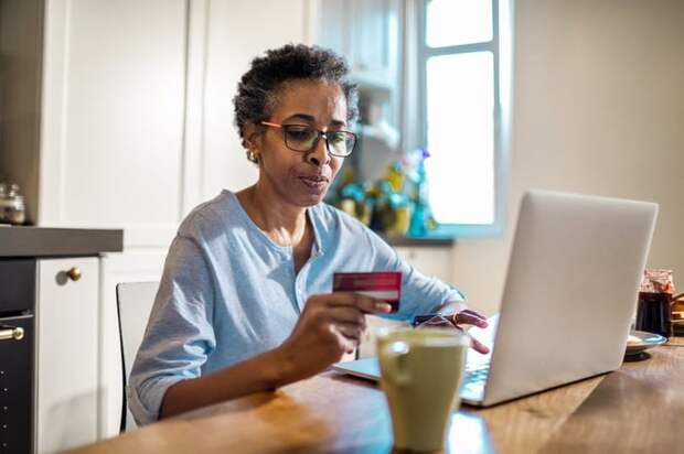 A person uses a credit card and laptop to purchase something online from their kitchen.