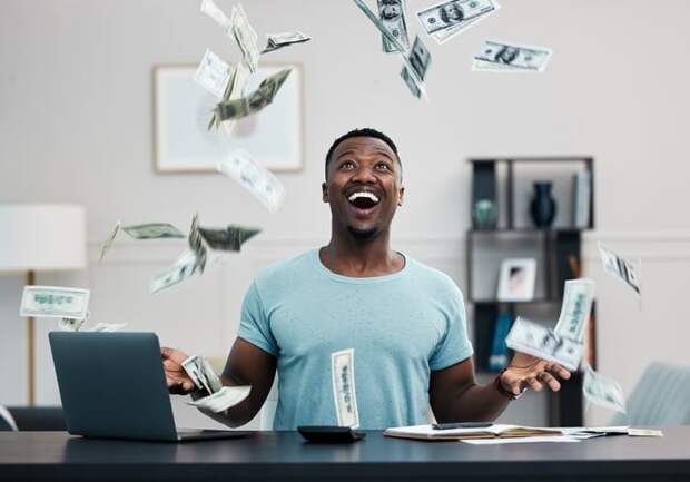 Investor sitting at a desk catching dollars falling out of the sky.