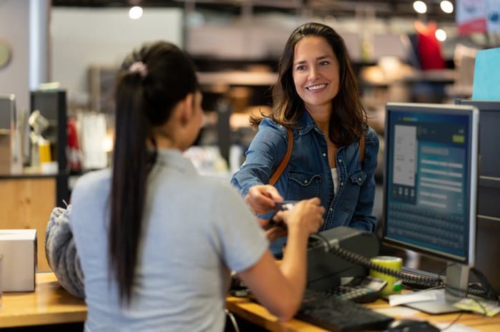 A woman handing her credit card to the employee at a cashier stand in a department store.