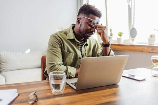A person at a laptop lifting their eyeglasses on their face.