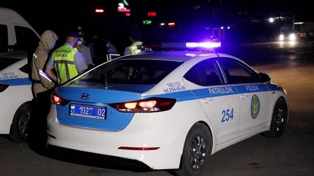 Полицейские стоят рядом со служебным авто с включенными мигалками Полицейские стоят рядом со служебным авто с включенными мигалками