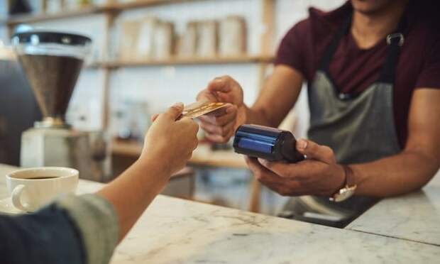 A hand holding a credit card out to a cashier behind the counter at a cafe.