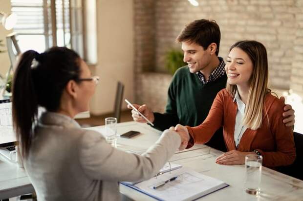 A man and woman signing home purchase papers while sitting at a desk and shaking hands with the realtor.