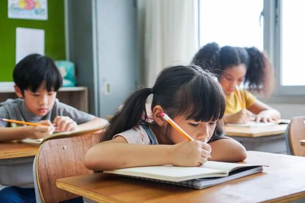 Three children sitting at desks and doing work in a classroom.