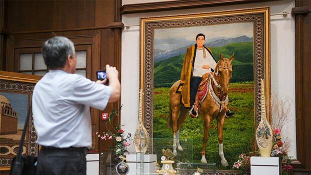 Мужчина фотографирует конный портрет президента Туркмении Гурбангулы Бердымухаммедова 