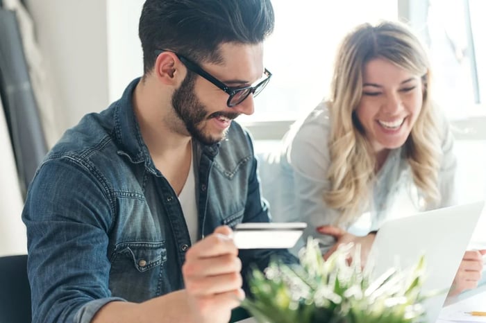 A man holding a credit card and a woman look at a laptop