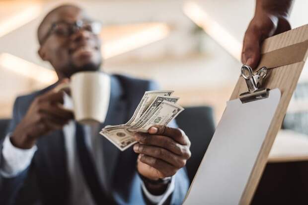 smiling young man holding a coffee mug and handing cash to a waiter