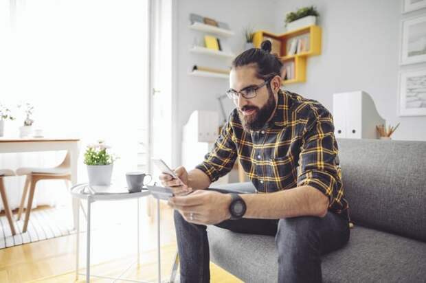 A man sitting on his couch and holding a credit card while looking up something on his phone.
