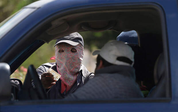 Вооруженный человек в маске проверяет личность водителя на контрольно-пропускном пункте на въезде в город Эль-Перикон, Мексика