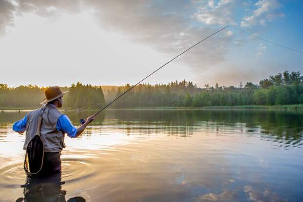 A man fly fishes at sunset after wading into a waterway