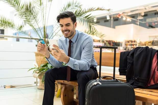 Traveler at airport with luggage, phone, and credit card.