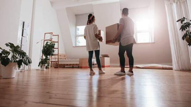 A young couple moving boxes and plants into a new apartment.