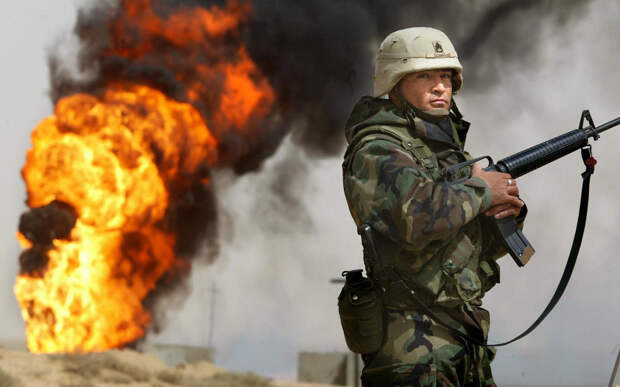 Американский солдат стоит рядом с горящей нефтяной скважиной в Румайле