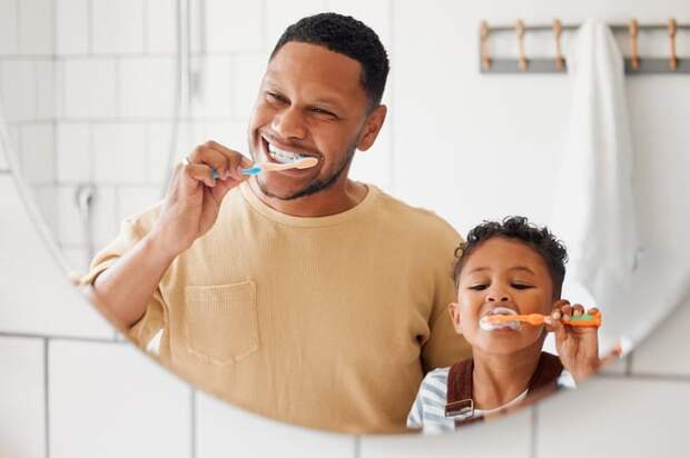 Adult and child brushing their teeth in front of bathroom mirror