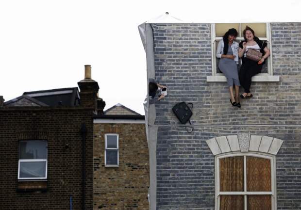 Visitors are seen in a reflection as they pose on Argentine artist Leonardo Erlich's optical illusion installation "Dalston House" in east London on June 26, 2013. The artwork, commissioned by the Barbican Gallery, uses mirrors to create the impression of a house on which people can play and pose for visual effect. (REUTERS / Luke MacGregor)